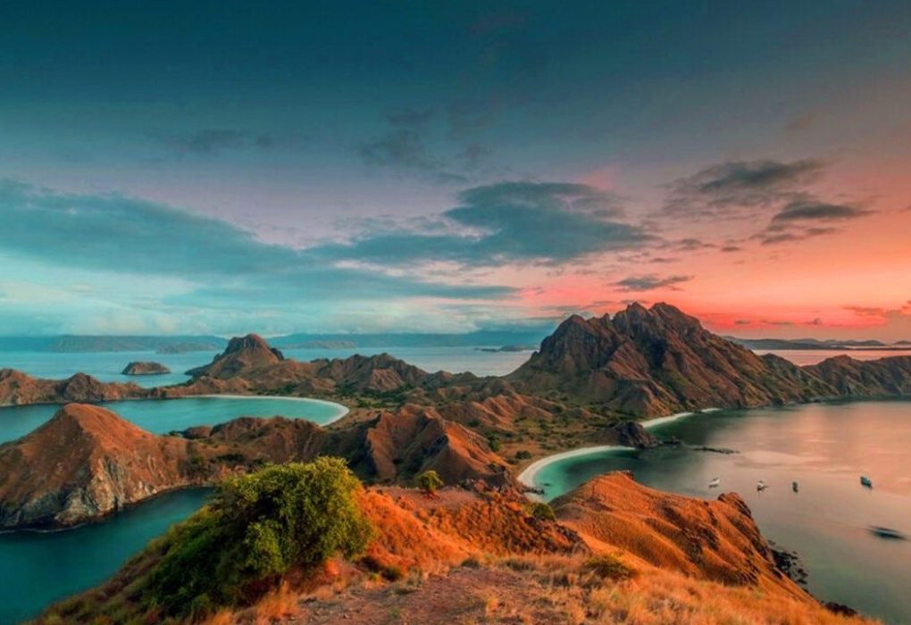 Panorama matahari terbenam yang menakjubkan di Labuan Bajo, dengan perahu-perahu yang berlabuh di pelabuhan dan langit yang berwarna oranye keemasan